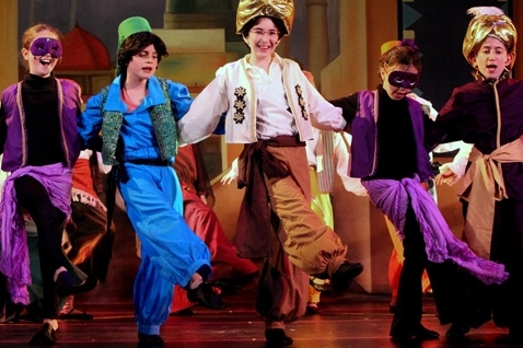 Actors in Aladdin costumes dancing on stage.